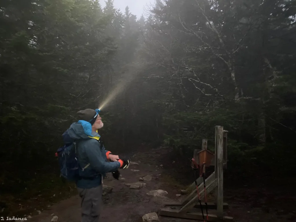 Hiker wearing head lamp_Camel's Hump hut clearing_10-28-2023_Joe Iadanza