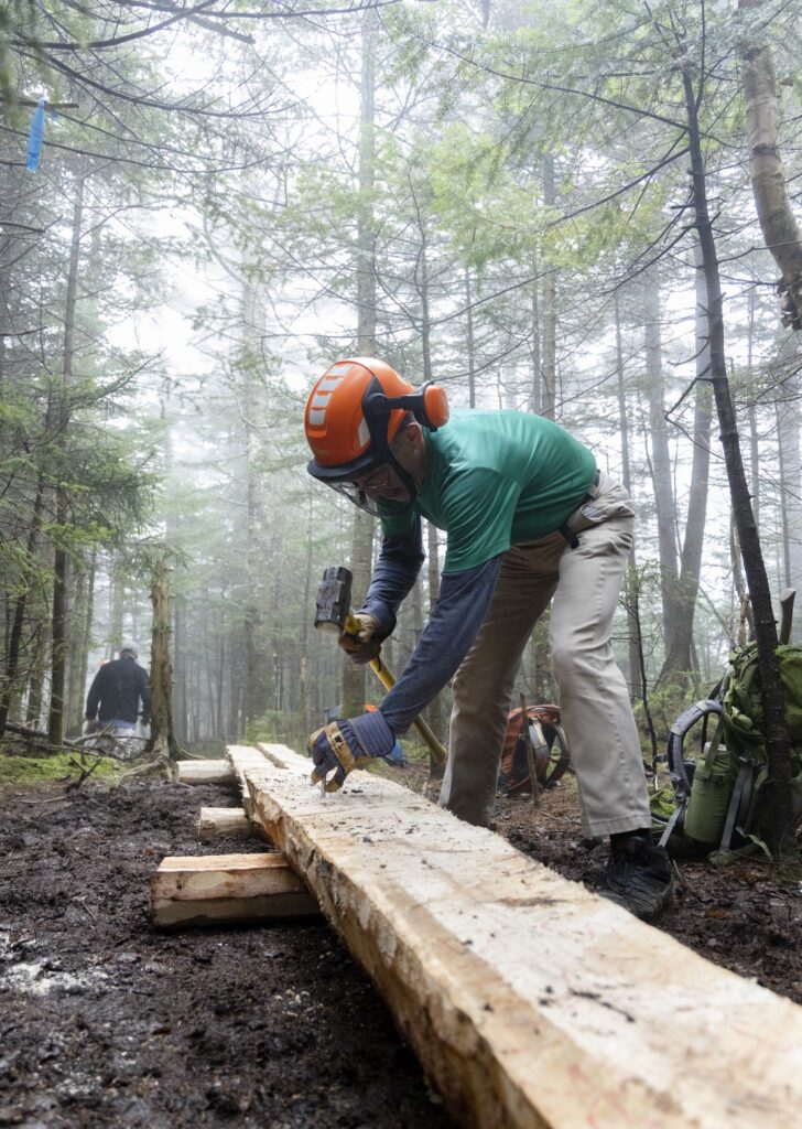 a volunteer bends over a wooden plank with a hammer