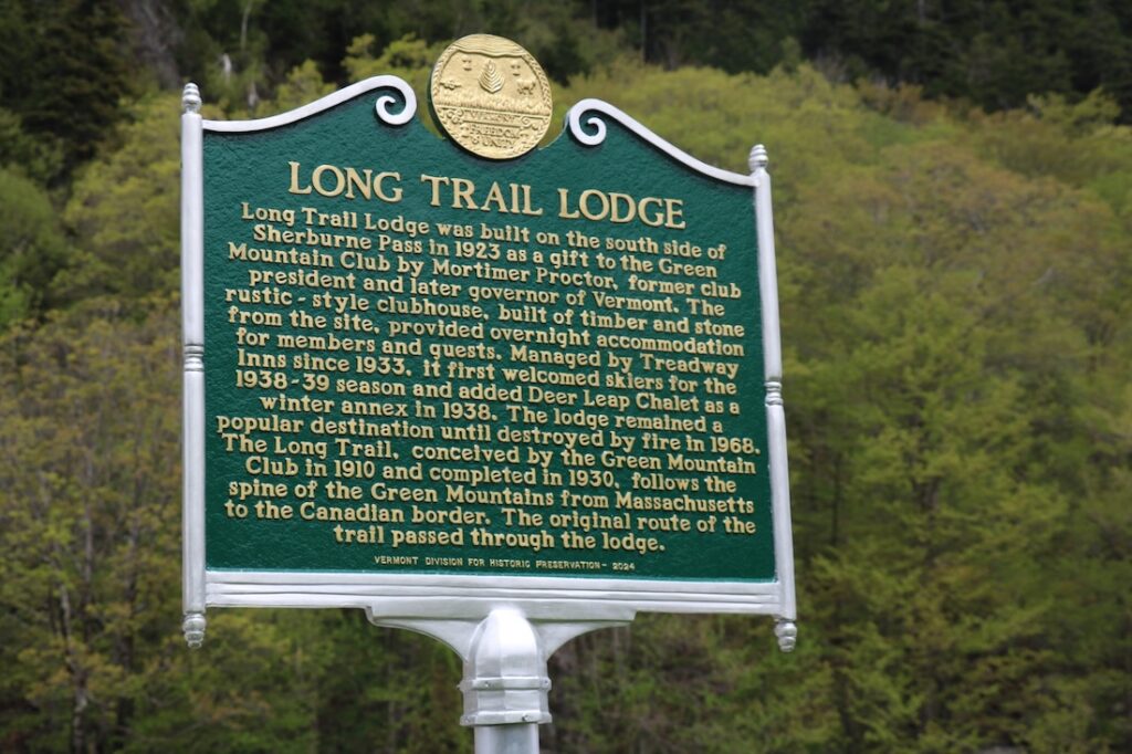 green sign with gold lettering with text detailing history of long trail lodge